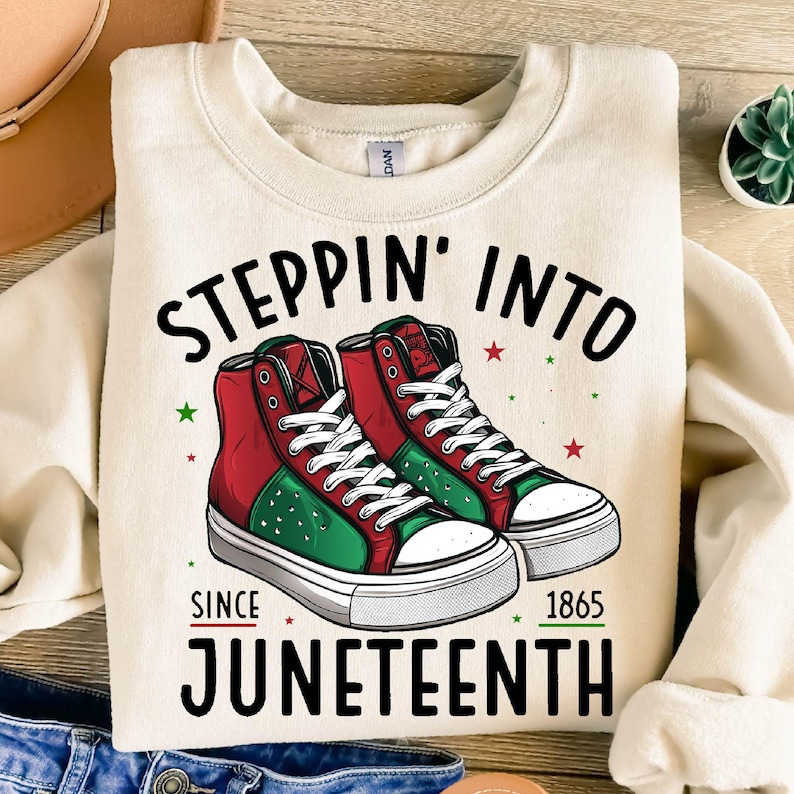 Może przedstawiać: Kremowa bluza z napisem "Steppin' Into Juneteenth Since 1865". Projekt przedstawia parę wysokich trampek w kolorze czerwonym, zielonym i czarnym. Trampki mają białe sznurowadła i podeszwy, z czerwonymi i zielonymi gwiazdami.