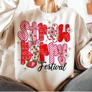 May include: White sweatshirt with a pink and red graphic that says "Strawberry Festival" with strawberries and flowers.