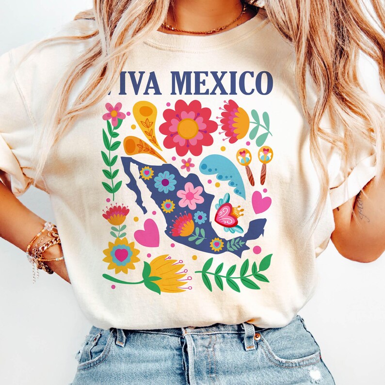 May include: A white t-shirt with a colorful graphic design featuring a stylized outline of Mexico with flowers, hearts, and maracas. The text "Viva Mexico" is printed on the shirt.