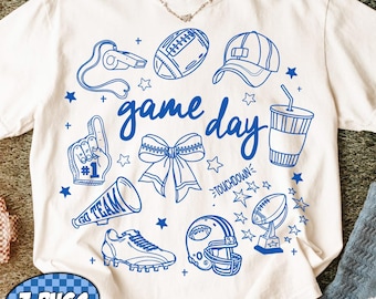 May include: White t-shirt with blue graphic illustrations of football-related items, including a football, helmet, and megaphone. The words "game day" are written in blue script. The shirt also has a blue and white PNG graphic.