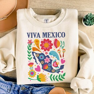 May include: A cream-colored sweatshirt with the text "Viva Mexico" in blue lettering. The sweatshirt features a colorful floral design with a blue outline of Mexico.