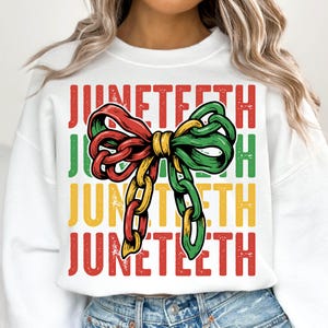 Może przedstawiać: Biała bluza z napisem "Juneteenth" w kolorze czerwonym, zielonym i ż&oacute;łtym. Centralnym elementem projektu jest kokarda w kształcie łańcucha w tych samych kolorach. Bluza ma swobodny styl.