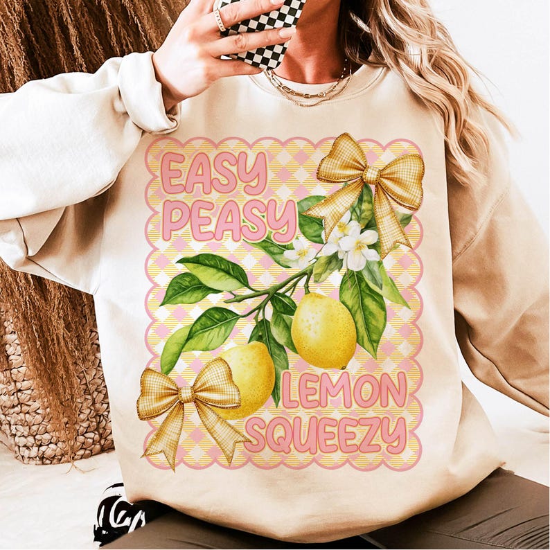 Pu&ograve; includere: Una felpa beige con un design grafico di limoni, fiori e fiocchi. Il testo "Easy Peasy Lemon Squeezy" &egrave; stampato sulla felpa.
