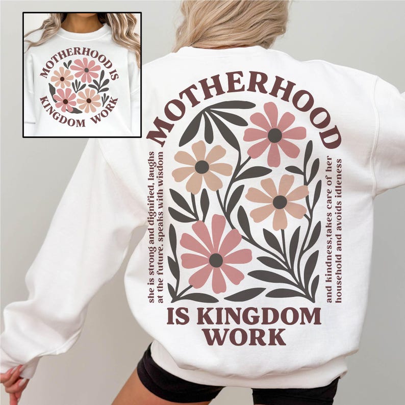 Puede incluir: Sudadera blanca con un dise&ntilde;o floral y el texto "Motherhood is Kingdom Work" impreso en la espalda. El texto es marr&oacute;n y las flores son rosas y marrones.