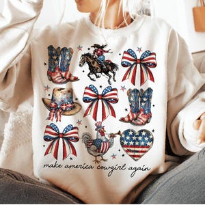 May include: White sweatshirt with a patriotic design featuring cowboy boots, bows, a horse and rider, a hat, a rooster, and a heart. The text "make america cowgirl again" is printed at the bottom.