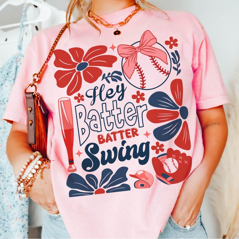 May include: Pink t-shirt with a baseball theme. The shirt features a baseball, bats, flowers, and the text "Hey Batter Batter Swing".