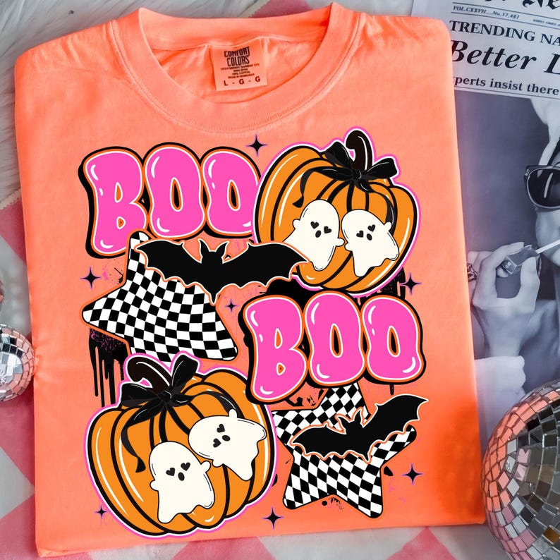 Puede incluir: Camiseta naranja Comfort Colors con un dise&ntilde;o de Halloween. El dise&ntilde;o incluye la palabra "BOO" en letras rosas, calabazas, fantasmas, murci&eacute;lagos y estrellas a cuadros. La camiseta es talla L-G.