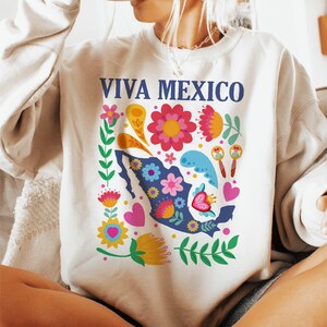 May include: A white sweatshirt with a blue and white graphic of a stylized map of Mexico surrounded by colorful flowers and the text "VIVA MEXICO".