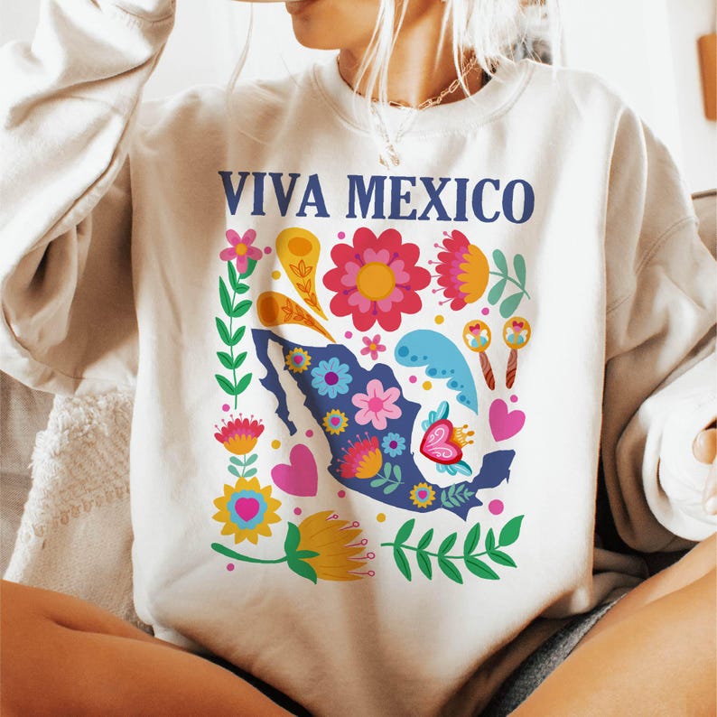 May include: A white sweatshirt with a blue and white graphic of a stylized map of Mexico surrounded by colorful flowers and the text "VIVA MEXICO".