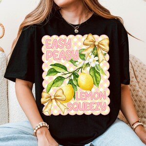 Pu&ograve; includere: Maglietta nera con un design grafico rosa e giallo con limoni, fiori e fiocchi. Il testo "Easy Peasy Lemon Squeezy" &egrave; stampato sulla maglietta.