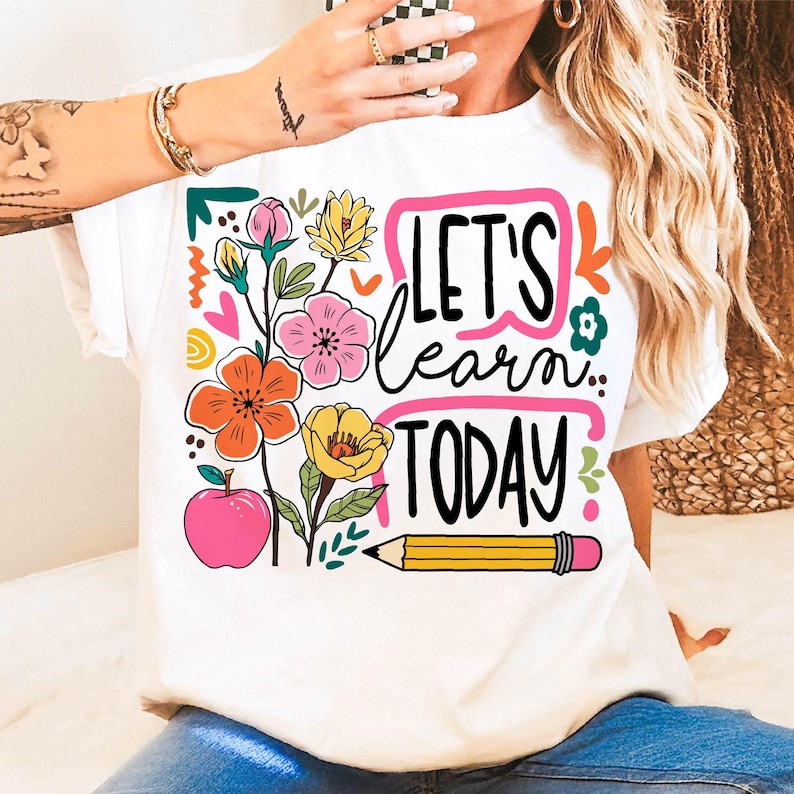 May include: White t-shirt with a colorful floral design and the text "LET'S learn TODAY". The design includes orange, pink, and yellow flowers, a pink apple, and a yellow pencil. A fun and educational theme.