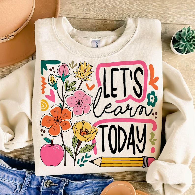 May include: Cream-colored sweatshirt with a colorful floral design and the text "LET'S learn TODAY". The graphic includes a pink apple, a yellow pencil, and various flowers in pink, orange, and yellow.