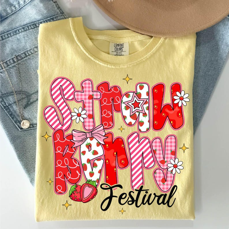 May include: A yellow t-shirt with a red and pink graphic that says "Strawberry Festival". The graphic is made up of letters with a strawberry and gingham pattern.