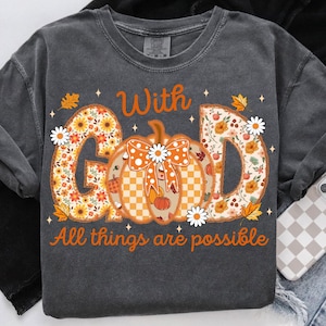 May include: Dark gray long-sleeve shirt with the words "With God All things are possible" in orange. The word "GOD" is filled with a floral pattern, and a pumpkin with a bow is in the center.