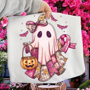 May include: A white Halloween-themed decorative cloth featuring a cartoon ghost with a pink bow, a pumpkin basket, and a pink ribbon. The ghost has purple eyes and is surrounded by pink bats. The ghost's dress has a floral pattern.