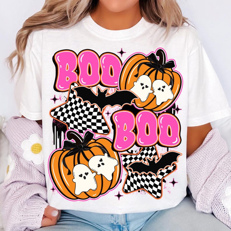 Puede incluir: Camiseta blanca con un dise&ntilde;o de Halloween. El dise&ntilde;o presenta la palabra "BOO" en letras rosas, calabazas naranjas, fantasmas blancos, murci&eacute;lagos negros y estrellas a cuadros. El dise&ntilde;o tiene un estilo retro y vintage.