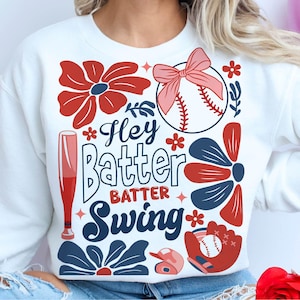 May include: White sweatshirt with a red, white, and blue baseball theme. The text on the shirt reads "Hey Batter Batter Swing".