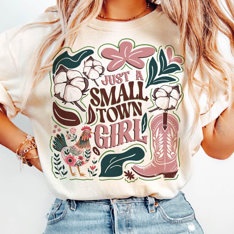 Pu&ograve; includere: Felpa color crema con un design grafico con la scritta "Just a Small Town Girl". Il design include uno stivale da cowboy rosa, fiori di cotone, un gallo ed elementi floreali nei toni del rosa, verde e marrone.