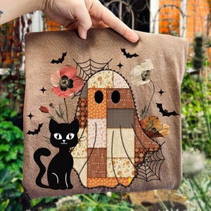 Könnte beinhalten: Ein braunes Halloween-Kissen mit einem Patchwork-Geist, einer schwarzen Katze, Blumen, Fledermäusen und Spinnennetzen. Der Geist hat ein Patchwork-Design in Orange-, Braun- und Cremetönen. Die Katze ist schwarz mit weißen Akzenten.
