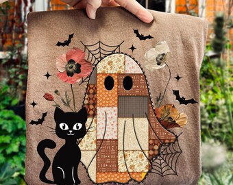 Pode incluir: Uma almofada castanha com tema de Halloween com um fantasma de patchwork, um gato preto, flores, morcegos e teias de aranha. O fantasma tem um design de patchwork em tons de laranja, castanho e creme. O gato é preto com detalhes brancos.