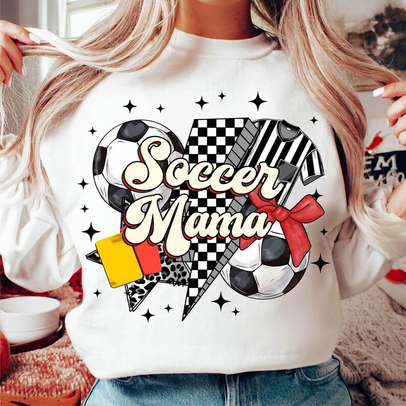 K&ouml;nnte beinhalten: Wei&szlig;es Sweatshirt mit einem Grafikdesign aus einem Fu&szlig;ball, einem Schiedsrichter und einer gelben Karte. Der Text "Soccer Mama" ist in einer Retro-Schrift.