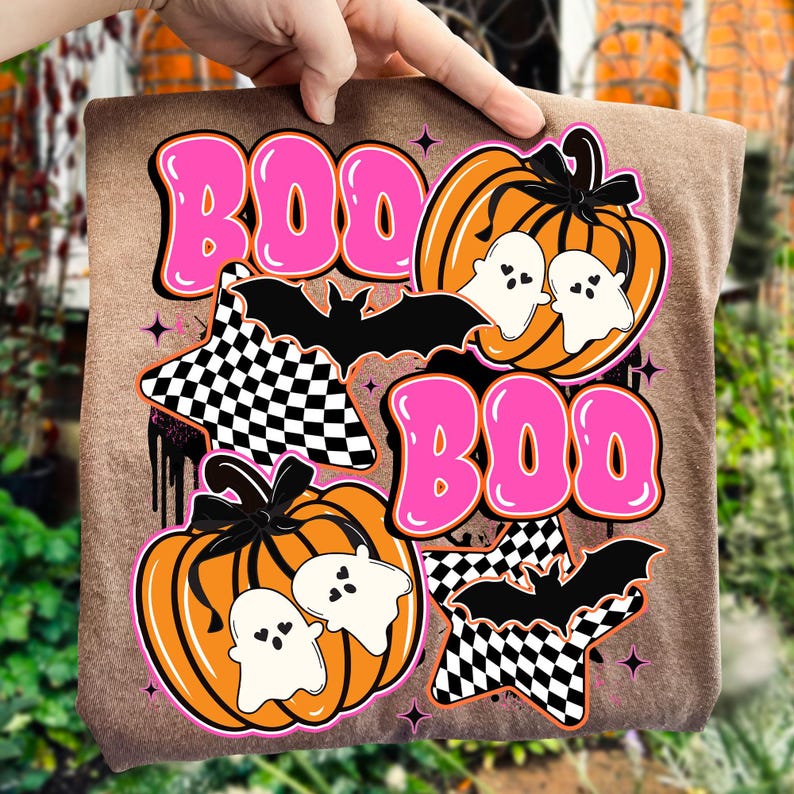 Puede incluir: Una camiseta marr&oacute;n con un dise&ntilde;o de Halloween. El dise&ntilde;o incluye la palabra "BOO" en letras rosas, calabazas naranjas, fantasmas blancos, murci&eacute;lagos negros y estrellas a cuadros. El tema general es espeluznante y divertido.