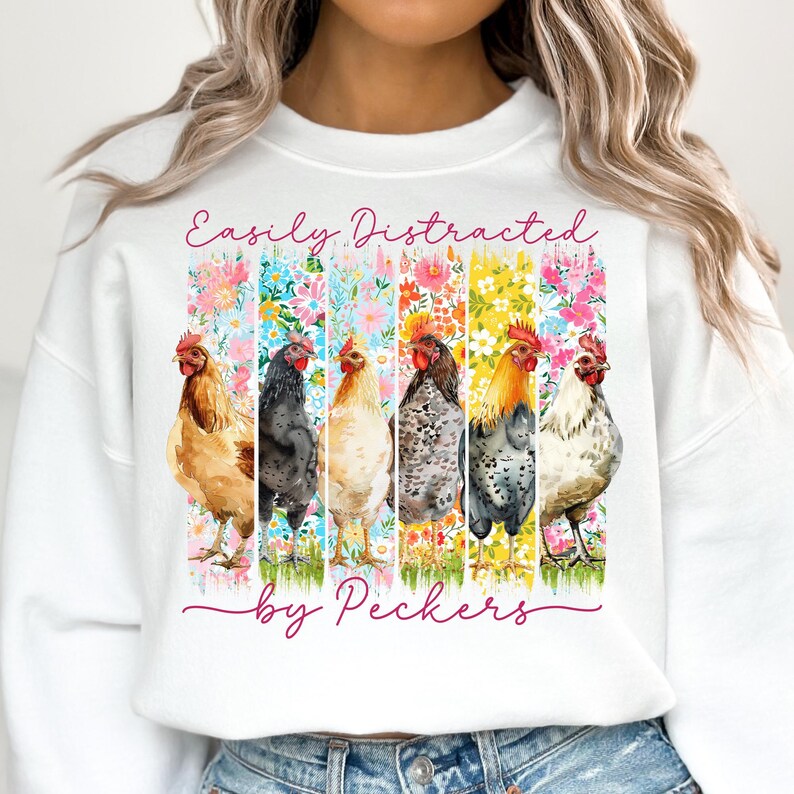 May include: White sweatshirt featuring a colorful graphic of six chickens in front of floral backgrounds. The text "Easily Distracted by Peckers" is written in a cursive font across the top and bottom of the design.