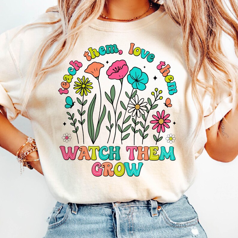 Puede incluir: Una camiseta blanca con un dise&ntilde;o gr&aacute;fico colorido que presenta flores y el texto "teach them, love them, watch them grow".