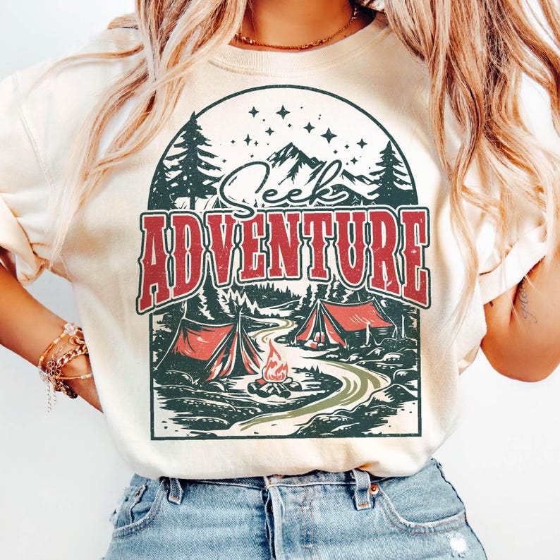 May include: A white t-shirt with a vintage-style graphic of a mountain scene with two tents, a campfire, and the text "Seek Adventure".