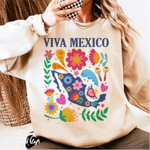 May include: A beige sweatshirt with a colorful floral design and the text "VIVA MEXICO" in blue letters. The design includes a silhouette of Mexico with flowers, hearts, and maracas.