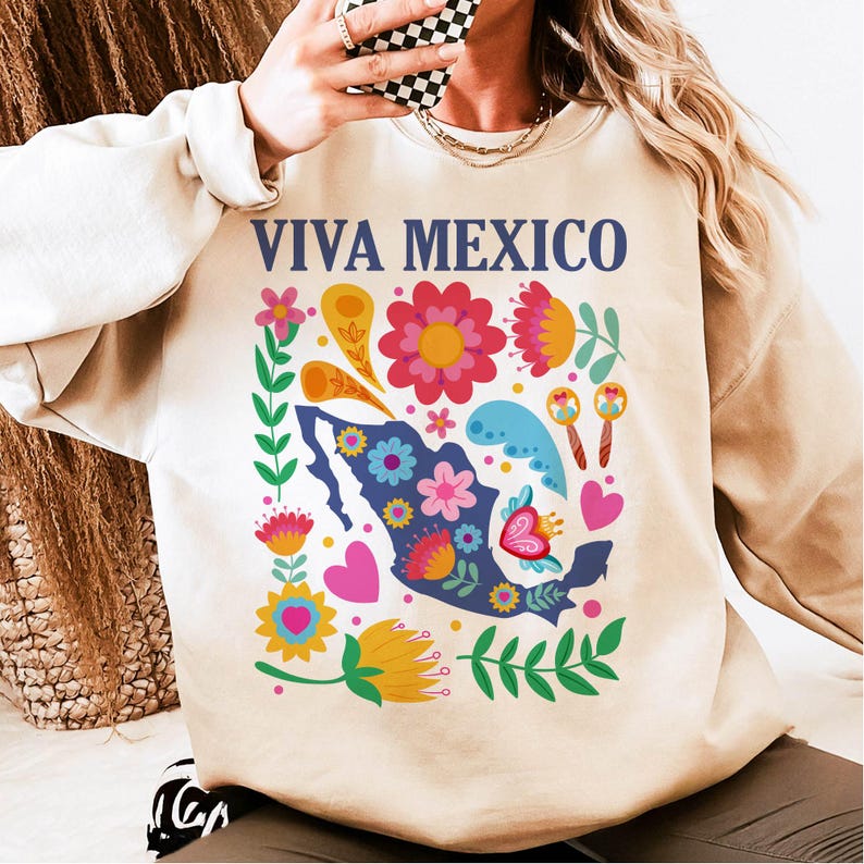 May include: A beige sweatshirt with a colorful floral design and the text "VIVA MEXICO" in blue letters. The design includes a silhouette of Mexico with flowers, hearts, and maracas.