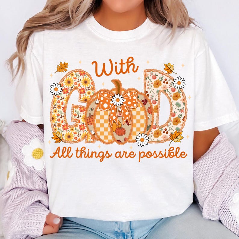 May include: White t-shirt with the text "With God All things are possible." The word "GOD" is designed with a floral pattern. A pumpkin with a bow is in the center. The shirt has a fall theme.