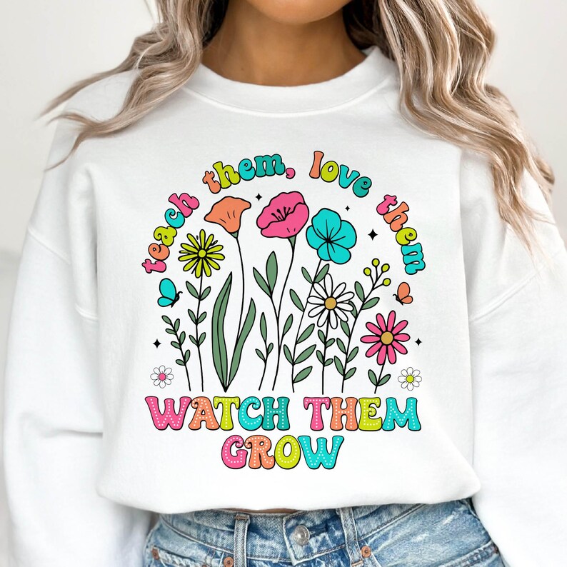 Puede incluir: Sudadera blanca con un dise&ntilde;o gr&aacute;fico colorido con flores y el texto "Teach them, love them, watch them grow".