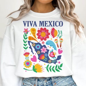 May include: White sweatshirt with a blue outline of Mexico and colorful flowers, hearts, and swirls. The text "VIVA MEXICO" is printed in blue on the front.