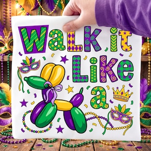 Könnte beinhalten: Weißes quadratisches Kissen mit dem Text "Walk it Like a" in bunten, gemusterten Buchstaben. Ein Ballon-Tier und Mardi-Gras-Masken verzieren das Kissen mit lila, grünen und goldenen Akzenten.