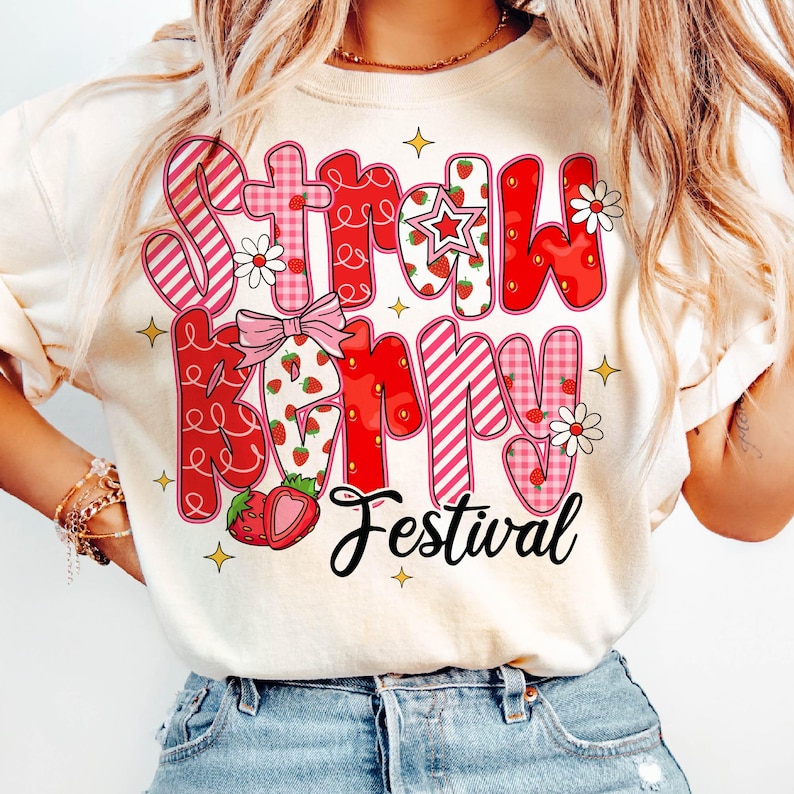 May include: A white t-shirt with a red and pink graphic design that says "Strawberry Festival". The design features strawberries, stars, and flowers.
