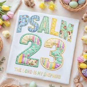 May include: White t-shirt with the text "PSALM 23" in patchwork letters and numbers. The numbers and letters are in various floral and patterned fabrics. The text "THE LORD IS MY SHEPHERD" is embroidered below.