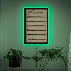 May include: A framed print of a display of wands with the text "Ollivanders Maker of Fine Wands since 382 BC" in a brown frame with a green light behind it.