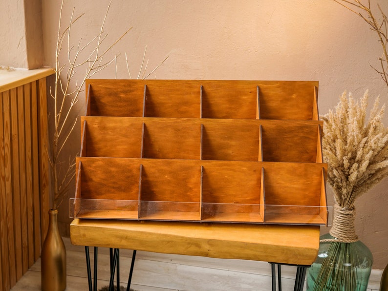 May include: A wooden display stand with 12 compartments, perfect for showcasing small items. The stand is made of natural wood and has a rustic look. It is sitting on a wooden table with black hairpin legs.