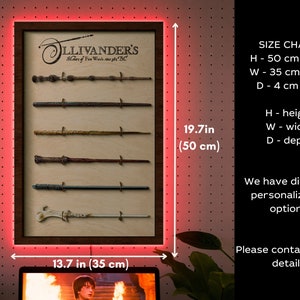 May include: A wooden frame with a light wood background and a dark wood border. The frame is displaying a collection of six wands, each with a different design. The frame is 50 cm tall and 35 cm wide. The text "Ollivander's Makers of Fine Wands since 382 BC" is printed on the frame. The frame is illuminated with red LED lights.