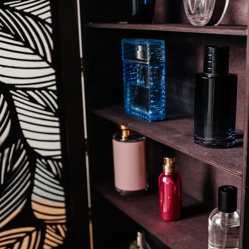 May include: A wooden shelf unit with five shelves, each holding various glass bottles of perfume. The bottles are in different colors, including blue, black, pink, and clear. The shelves are dark brown and the unit is made of wood.