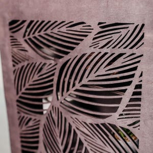 May include: A close-up of a wooden panel with a decorative cut-out design of overlapping leaves. The leaves are cut in a repeating pattern of thin lines, creating a geometric and intricate design.