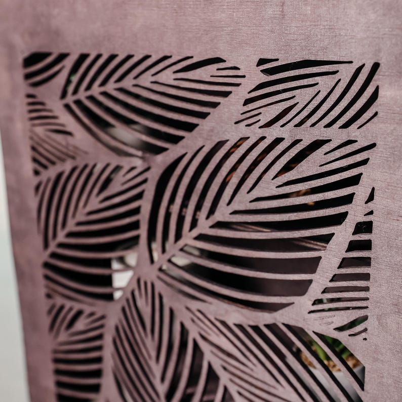 May include: A close-up of a wooden panel with a decorative cut-out design of overlapping leaves. The leaves are cut in a repeating pattern of thin lines, creating a geometric and intricate design.