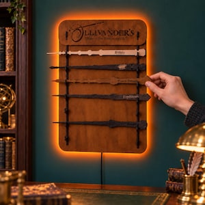 Könnte beinhalten: Ein rechteckiges Wanddisplay aus braunem Holz mit Hintergrundbeleuchtung und der Aufschrift Ollivander's Makers of Fine Wands since 382 BC. Das Display hält fünf horizontale Zauberstäbe, die jeweils mit einem Zauberspruch wie Riddikulus, Expecto Patronum und Expelliarmus graviert sind.