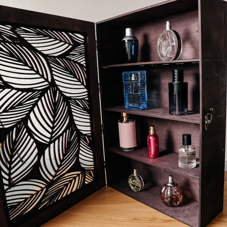 May include: A wooden cabinet with a decorative leaf pattern on the door, open to reveal shelves filled with various bottles of perfume and cologne. The bottles are arranged in rows on the shelves, with some bottles in clear glass and others in opaque glass.