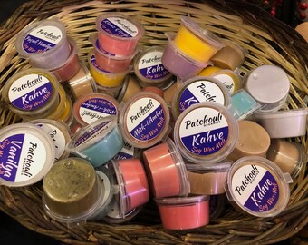 May include: A collection of small, round, clear containers filled with colorful wax melts. The containers have labels with the text "Patchouli Organics" and "Kahve Soy Wax Melt".