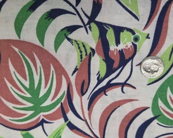 May include: A white fabric featuring a repeating pattern of tropical leaves in green and muted red, interspersed with dark blue angelfish. A silver United States dime is placed on the fabric to provide a sense of scale for the printed design.