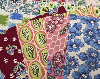 May include: A collection of fabric swatches featuring various patterns including blue flowers, pink honeycomb with floral motifs, green and orange abstract shapes, and a deep red background with small white and green floral designs.