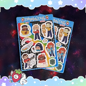 Op de afbeelding: Twee stickerbladen met kleurrijke cartoonillustraties van personages en zinnen. De stickers bevatten afbeeldingen van mensen, een kat en zinnen als "Touch Grass" en "Boldly Go". De bladen zijn geplaatst tegen een ruimte-thema achtergrond.