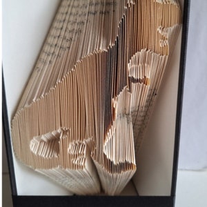 May include: A book folded into the shape of a dog. The book is open and the dog is facing the right side of the image. The book is brown and the pages are folded into a 3D shape. The book is sitting on a black surface. The word "Pattern" is printed in black on a gray background below the image.